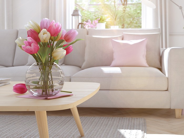 Living room with neutral colored furniture decorated with bright pink accent pillows and flowers.